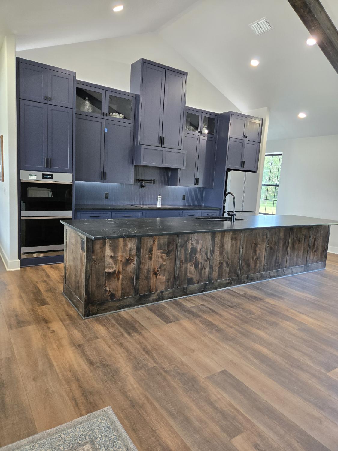 Wide view of a navy kitchen with a long wood-clad island and dark stone
