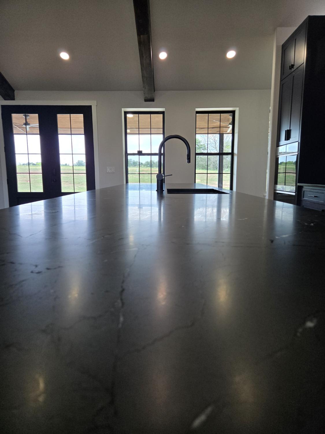 Looking down a Black Diamond quartzite island toward black-grid windows and doors