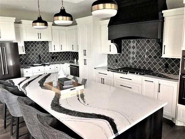 Spacious kitchen with white cabinetry, black appliances, and a large island featuring a black and white marble countertop. Three pendant lights hang above the island. The backsplash is black tile with a diamond pattern.