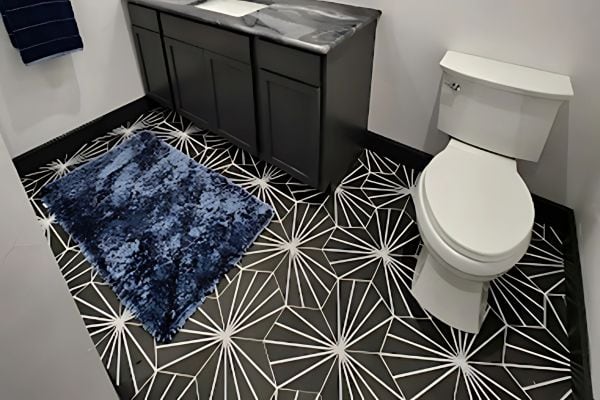 Bathroom with a geometric black-and-white tiled floor, a white toilet, a black vanity with a marble countertop, and a dark blue textured rug on the floor.