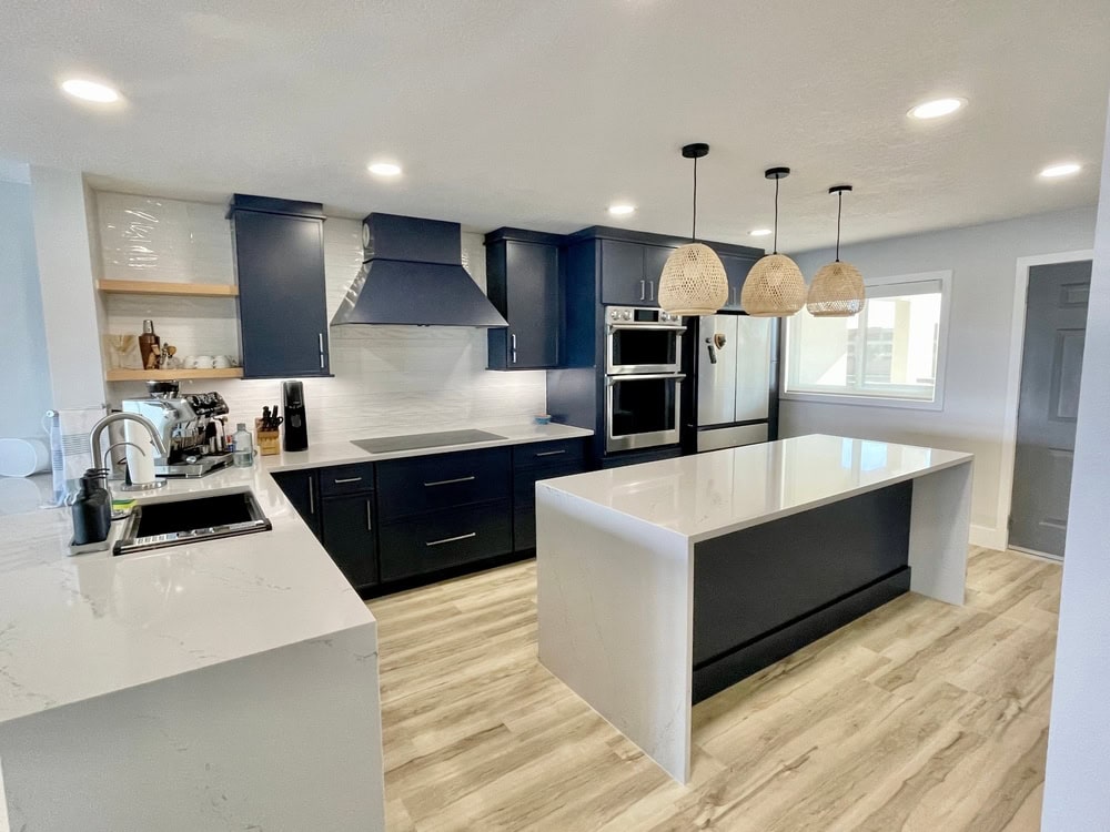 Modern kitchen with black cabinets, stainless steel appliances, and a white marble island. Three woven pendant lights hang over the island. Light wood flooring and a window provide a bright, clean look.