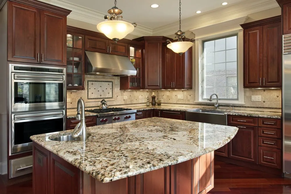 Luxurious kitchen featuring dark wood cabinets, granite countertops, an island with a prep sink, stainless steel appliances, and pendant lighting. A large window brings in natural light, highlighting the elegant design.